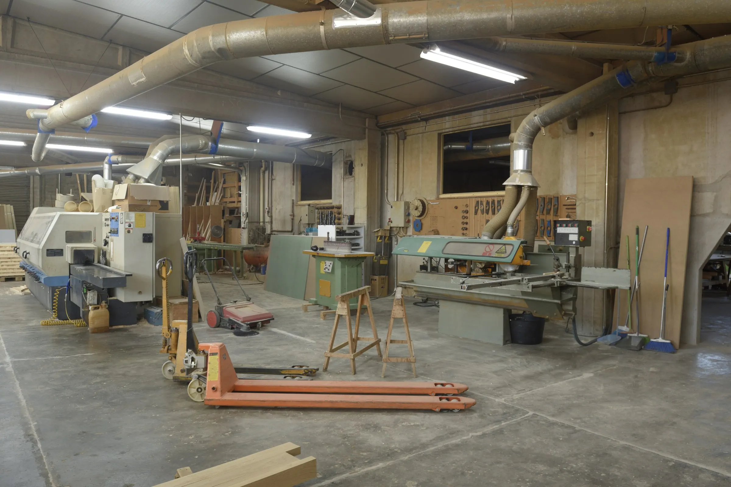 Atelier de menuiserie : machines à bois, tréteaux et transpalette sur un sol en béton