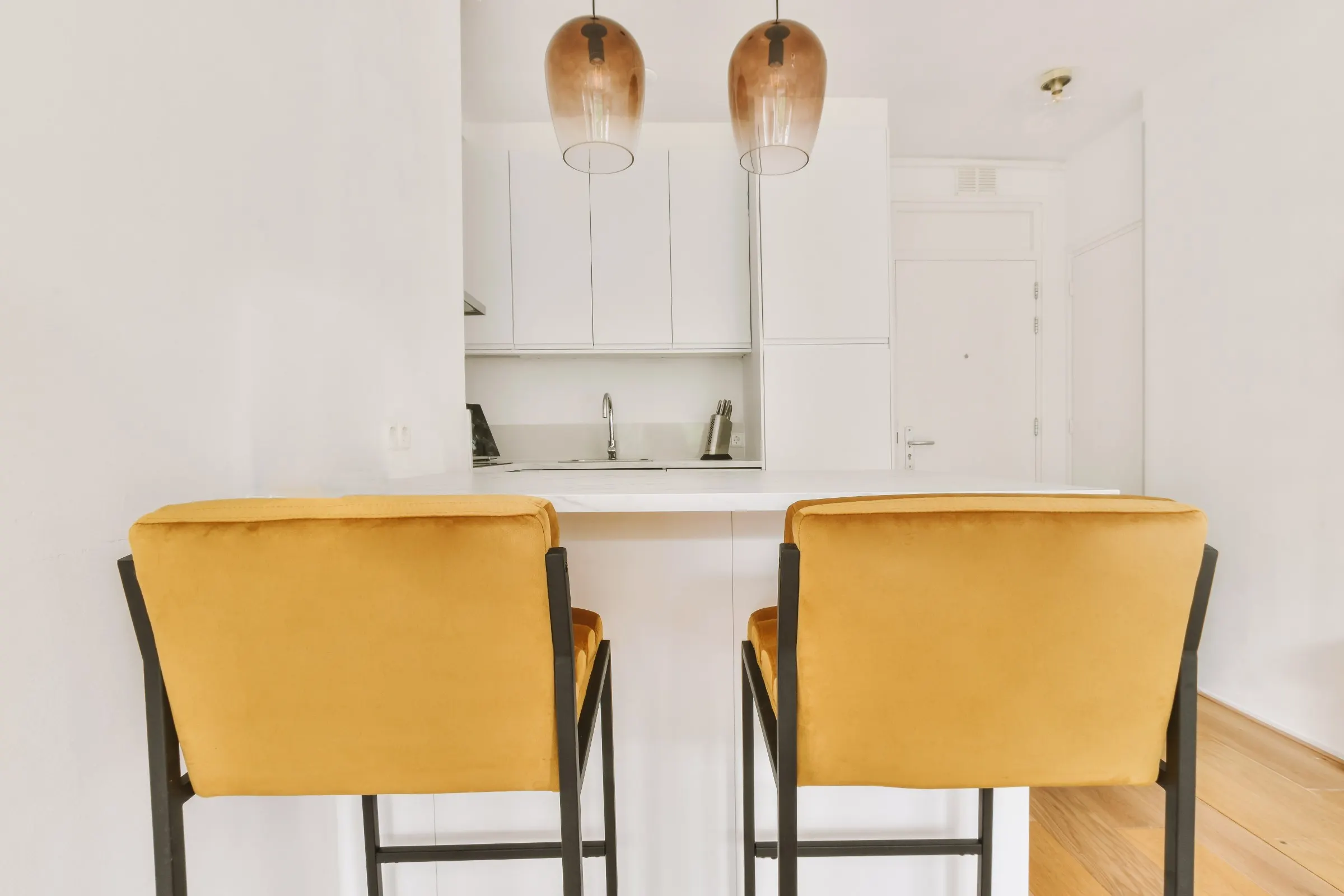 Coin cuisine blanc d'un petit appartement, deux chaises hautes jaunes devant le comptoir