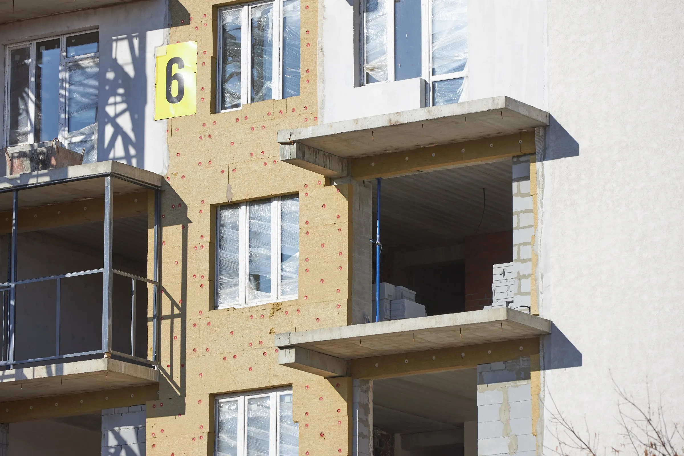 Façade d'immeuble en chantier couverte de panneaux d'isolant fixés par chevilles, fenêtres encore sous film