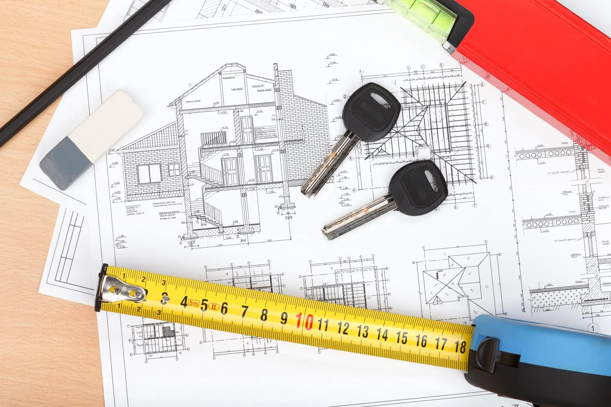 Plans de maison imprimés sur une table, avec un mètre ruban, un compas, un rapporteur et une tasse de café
