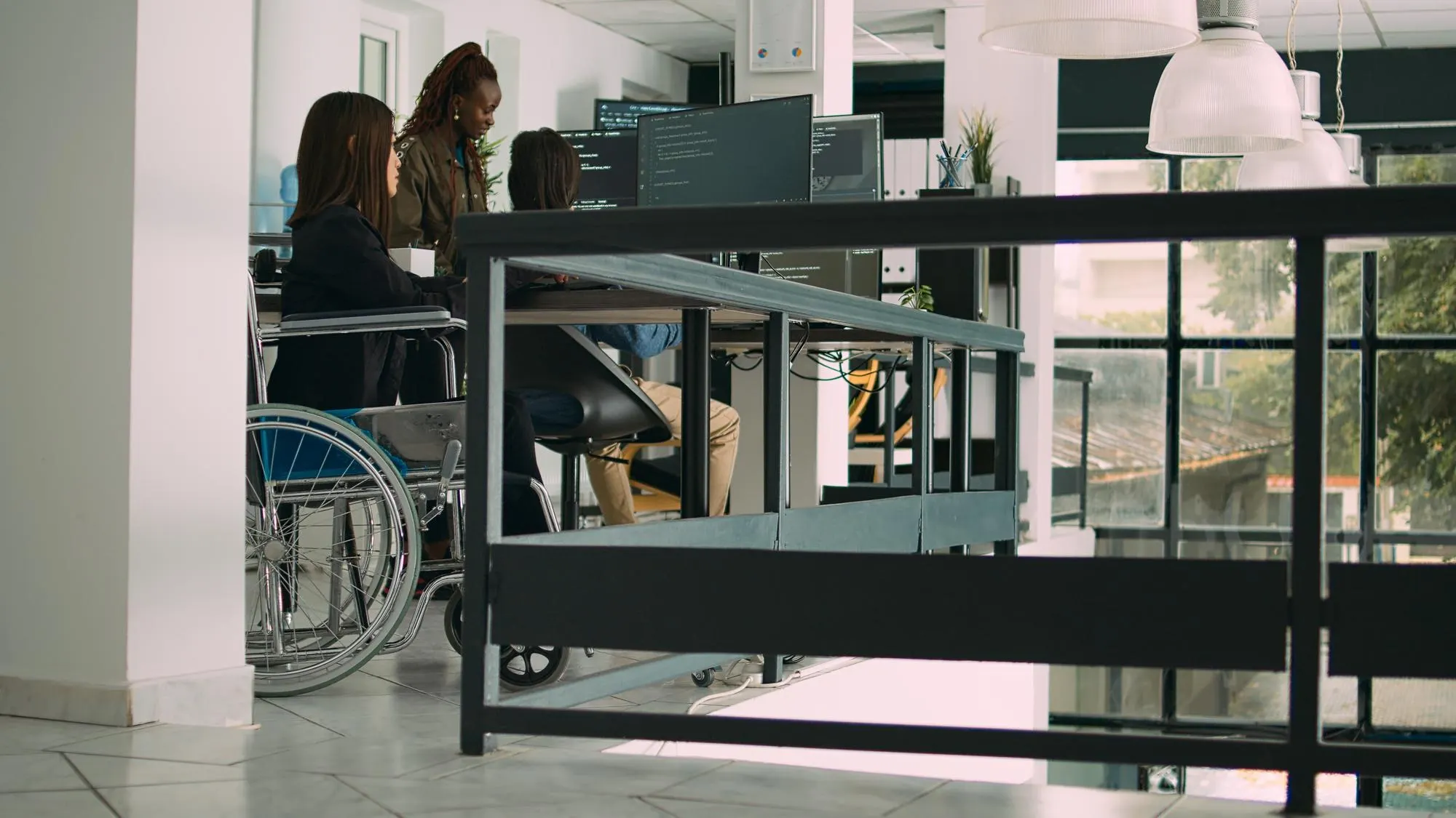 Dans un bureau clair, une femme en fauteuil roulant travaille devant un écran avec deux collègues